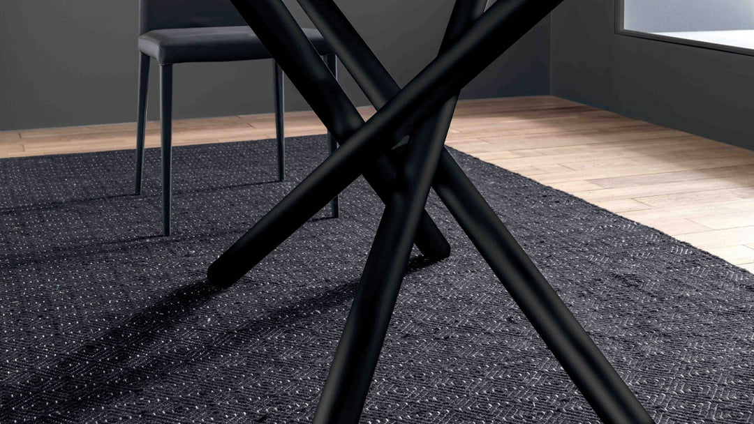 London close-up of black metal chair legs on a textured blue rug with a gray wall and wooden floor in the background.