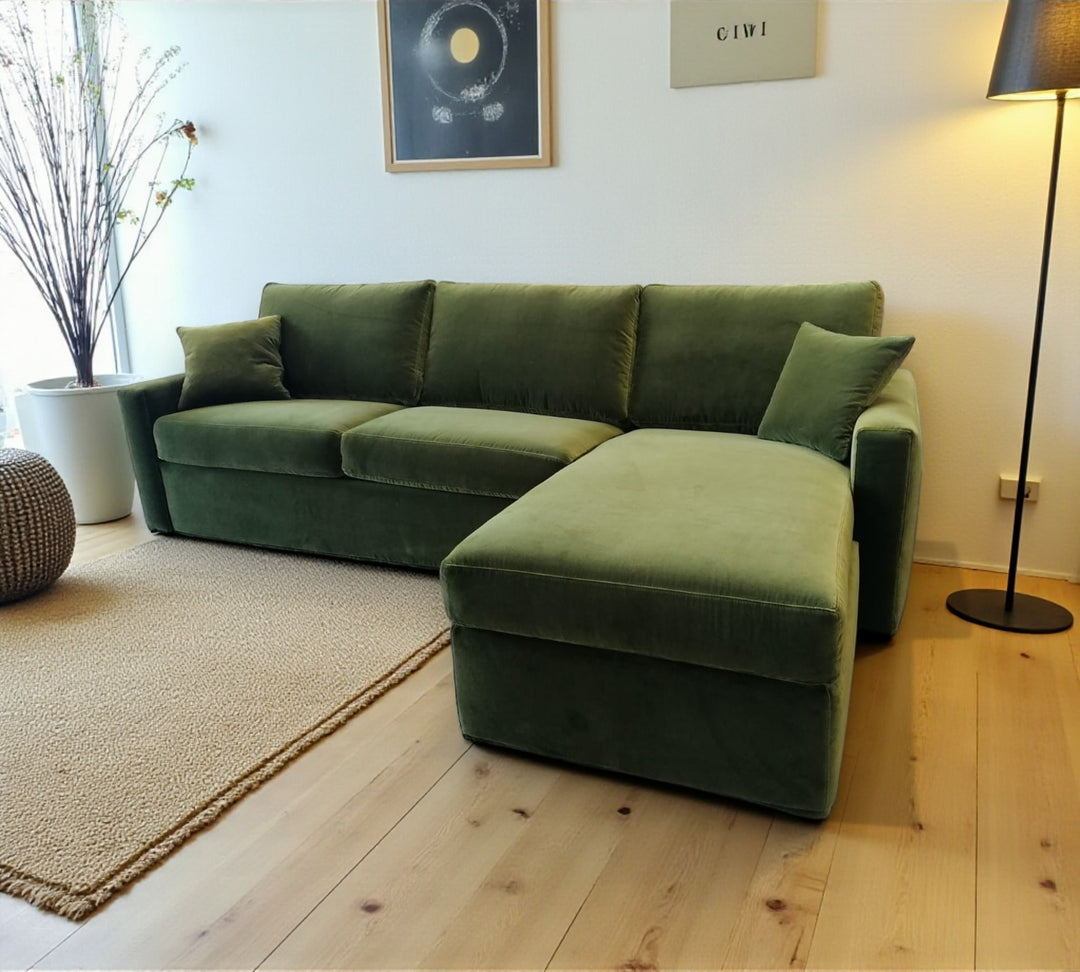 Green sectional sofa bed in a living room with a plant and lamp.